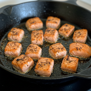 Blackened salmon bites sizzling in a skillet.