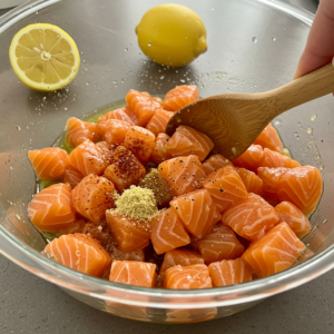 Salmon cubes being seasoned with olive oil, paprika, and garlic.