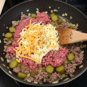 Ground beef, onions, and cheese melting together in a skillet for cheeseburger egg rolls.